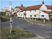 TG0442 : The Wiveton Bell pub and signpost by Andy Parrett