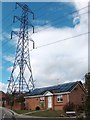 House with solar panels beneath electricity pylon at Ormes Meadow