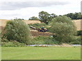 Tracked tractor ploughing by stream with willow trees